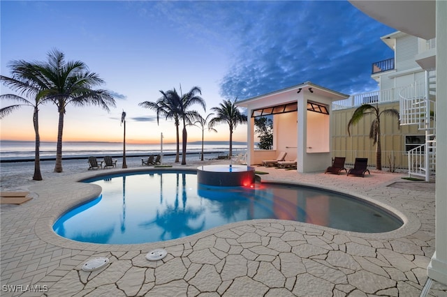 pool at dusk featuring a patio and a water view