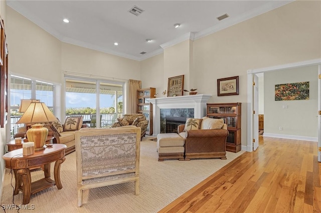 living room with a tiled fireplace, ornamental molding, and light wood-type flooring