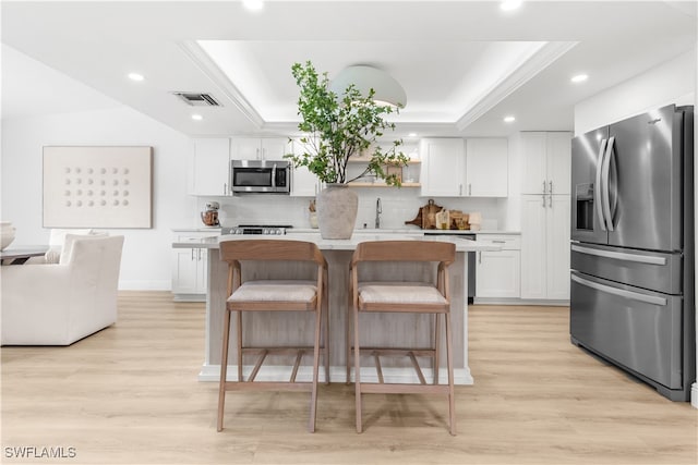 kitchen with white cabinetry, a tray ceiling, a center island, and appliances with stainless steel finishes