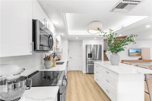 kitchen with stainless steel appliances, white cabinets, a center island, light hardwood / wood-style flooring, and a tray ceiling