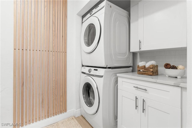 clothes washing area featuring stacked washing maching and dryer and cabinets