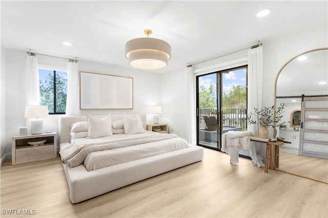 bedroom with access to exterior, light hardwood / wood-style floors, and a barn door