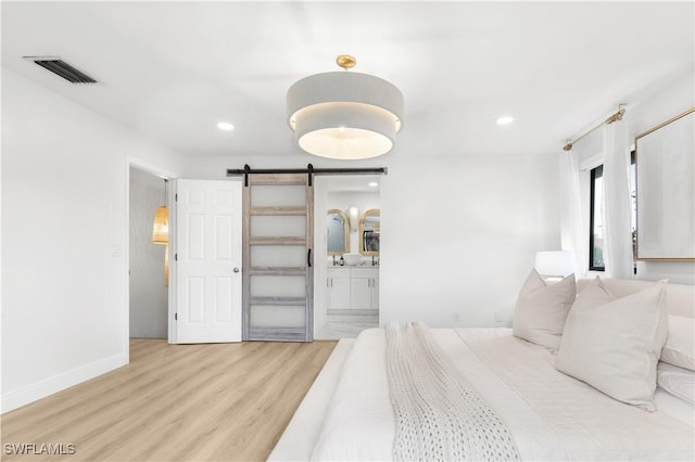 bedroom featuring light wood-type flooring, ensuite bathroom, and a barn door