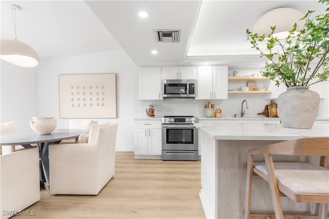 kitchen featuring stainless steel appliances, white cabinetry, decorative light fixtures, and light stone countertops