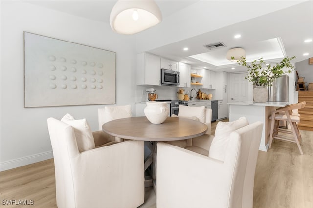 dining room featuring a raised ceiling, light hardwood / wood-style flooring, and sink