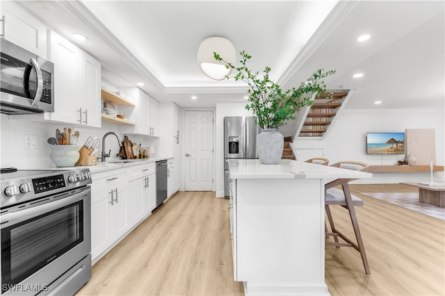 kitchen with stainless steel appliances, sink, white cabinetry, ornamental molding, and a breakfast bar area