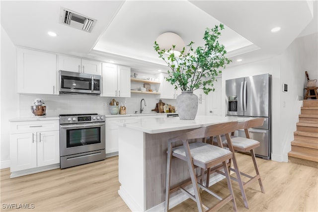 kitchen with stainless steel appliances, white cabinetry, light wood-type flooring, and a tray ceiling