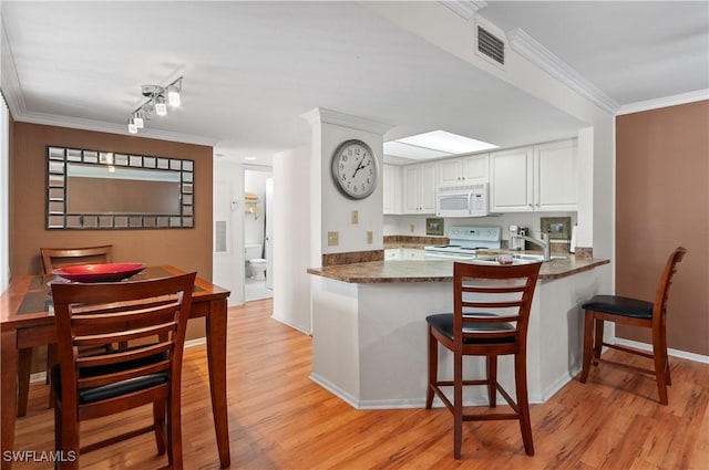 kitchen with white appliances, visible vents, white cabinets, dark countertops, and a peninsula