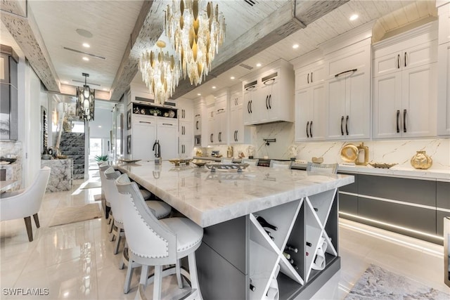 kitchen featuring white cabinets, light stone countertops, beamed ceiling, and a large island