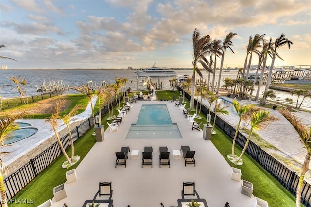 pool at dusk featuring a water view and a hot tub