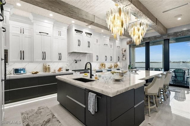 kitchen with beamed ceiling, tasteful backsplash, white cabinetry, a sink, and a spacious island
