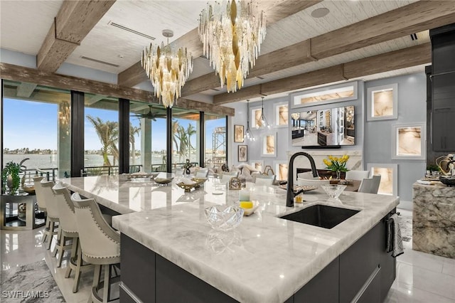 kitchen featuring a sink, beamed ceiling, a spacious island, and light stone countertops