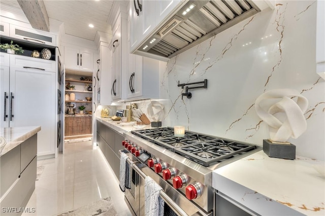 kitchen featuring light stone counters, premium range hood, white cabinets, decorative backsplash, and range with two ovens
