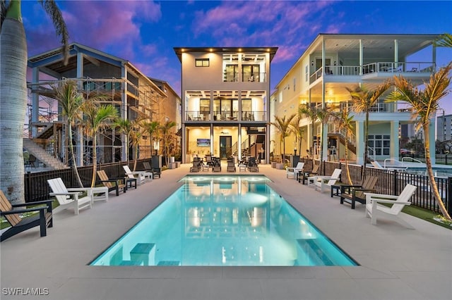 back of house at dusk featuring a patio, a community pool, and fence