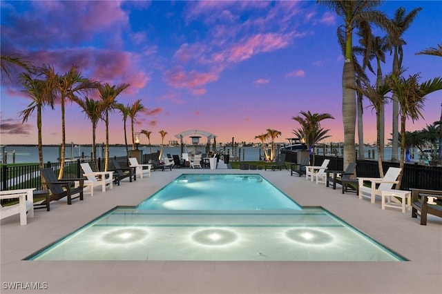 view of swimming pool featuring a water view, fence, and a patio