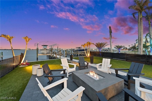 patio terrace at dusk with a water view, an outdoor fire pit, a lawn, boat lift, and a boat dock