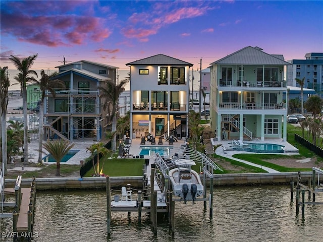 back of house at dusk featuring a water view, a patio area, boat lift, and stairs