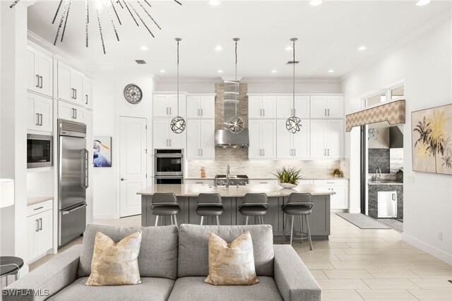 kitchen featuring built in appliances, a center island with sink, decorative light fixtures, and a breakfast bar