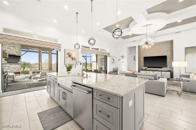 kitchen featuring stainless steel dishwasher, decorative light fixtures, a center island with sink, and sink