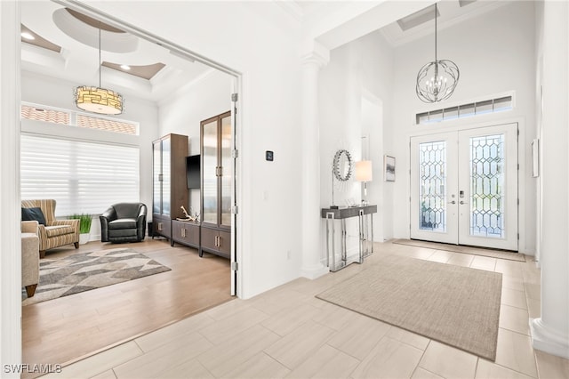 tiled foyer featuring french doors, coffered ceiling, crown molding, a chandelier, and a high ceiling