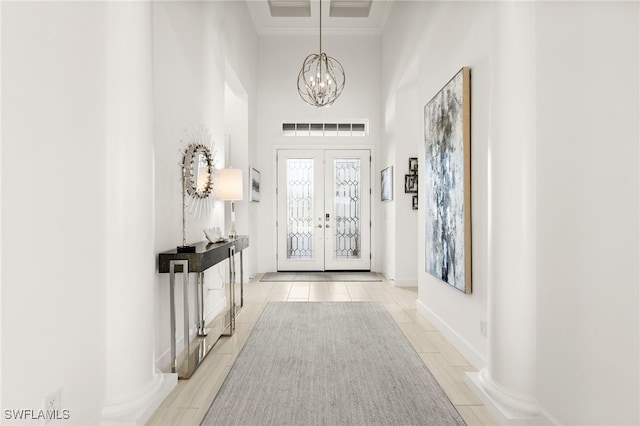 foyer with french doors, a towering ceiling, light tile patterned floors, and an inviting chandelier