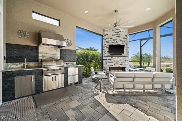 view of patio / terrace featuring ceiling fan, sink, an outdoor living space with a fireplace, exterior kitchen, and grilling area