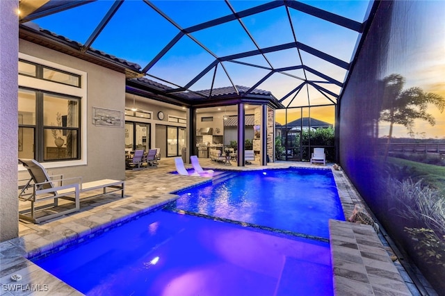 pool at dusk featuring a lanai, pool water feature, and a patio