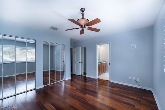 unfurnished bedroom featuring dark wood-type flooring, multiple closets, ensuite bath, and ceiling fan