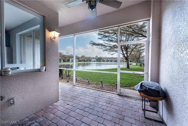 sunroom featuring ceiling fan and a water view