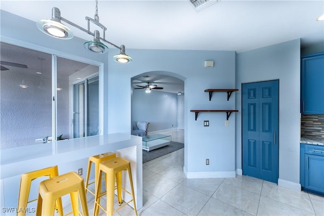 kitchen with tasteful backsplash, ceiling fan, a breakfast bar, light tile patterned floors, and blue cabinets