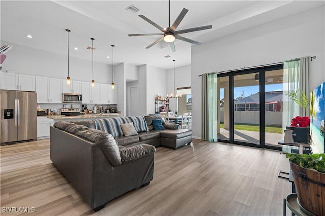 living room with a wealth of natural light, a high ceiling, ceiling fan with notable chandelier, and light wood-type flooring