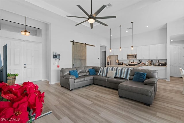 living room with a barn door, ceiling fan, a high ceiling, and light wood-type flooring