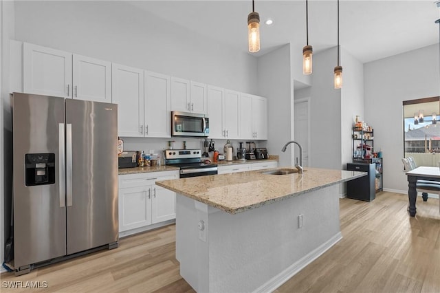 kitchen featuring sink, an island with sink, appliances with stainless steel finishes, decorative light fixtures, and white cabinetry