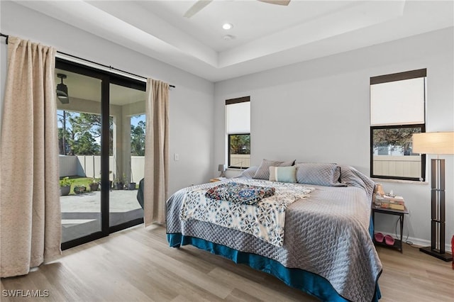 bedroom with access to outside, ceiling fan, a tray ceiling, and light hardwood / wood-style floors