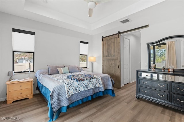 bedroom featuring hardwood / wood-style floors, a barn door, a raised ceiling, and ceiling fan