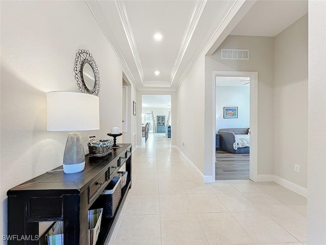 corridor featuring a tray ceiling, crown molding, and light tile patterned floors