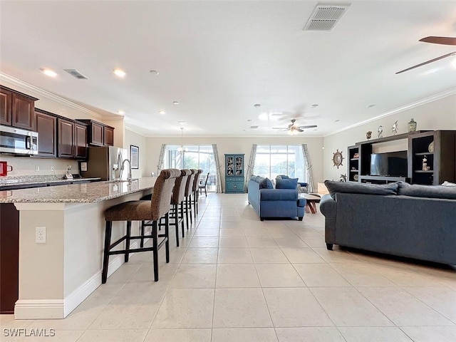 kitchen featuring dark brown cabinetry, appliances with stainless steel finishes, a breakfast bar, light tile patterned floors, and ornamental molding