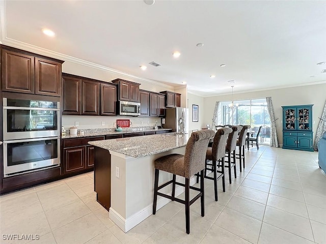 kitchen featuring a breakfast bar, appliances with stainless steel finishes, a center island with sink, and ornamental molding