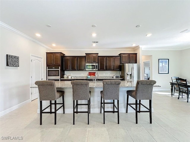 kitchen with light stone countertops, appliances with stainless steel finishes, a kitchen breakfast bar, dark brown cabinetry, and an island with sink