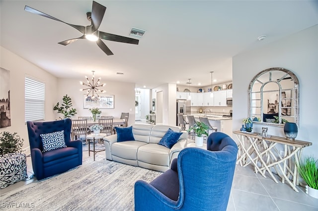 living room with light tile patterned flooring, visible vents, and ceiling fan with notable chandelier