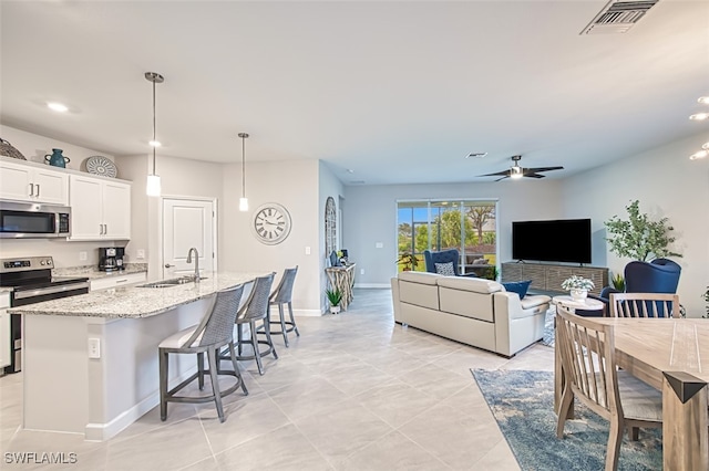 kitchen featuring appliances with stainless steel finishes, an island with sink, sink, white cabinets, and hanging light fixtures