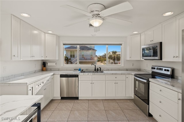 kitchen featuring sink, light tile patterned floors, appliances with stainless steel finishes, light stone countertops, and white cabinets