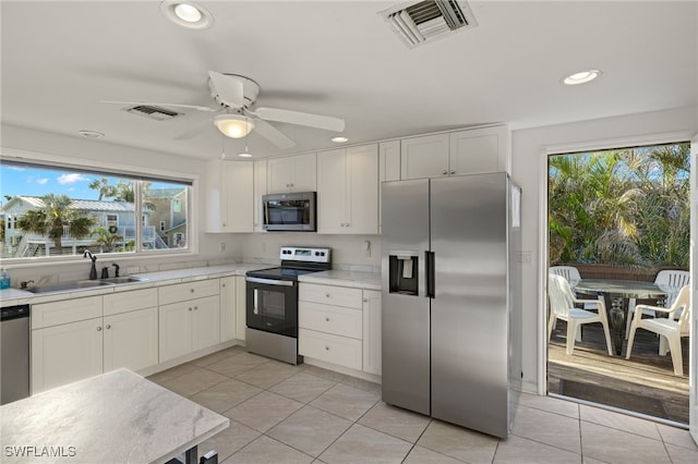 kitchen featuring stainless steel appliances, sink, light tile patterned floors, a healthy amount of sunlight, and white cabinets