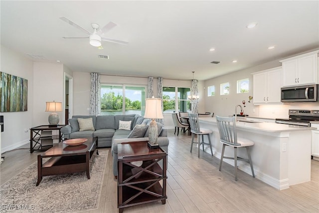 living room featuring ceiling fan with notable chandelier, light hardwood / wood-style floors, and sink