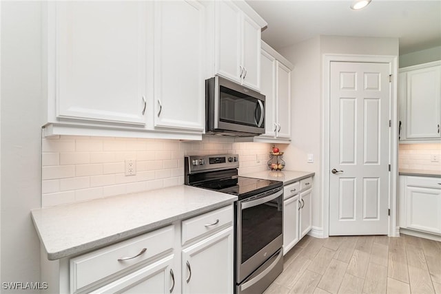 kitchen with decorative backsplash, light hardwood / wood-style floors, light stone counters, white cabinetry, and stainless steel appliances