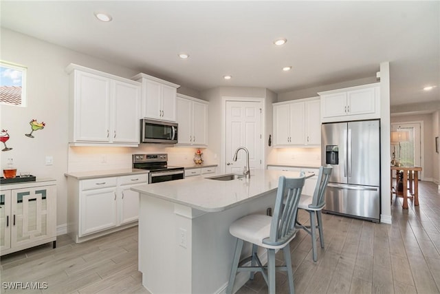 kitchen featuring appliances with stainless steel finishes, sink, a center island with sink, white cabinets, and light hardwood / wood-style floors