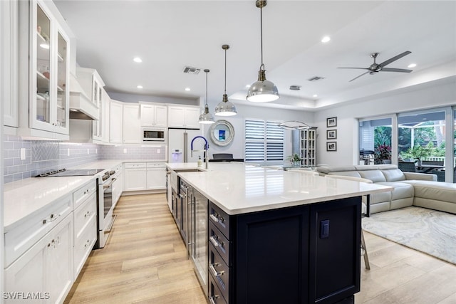 kitchen featuring light wood-type flooring, white appliances, pendant lighting, white cabinetry, and an island with sink