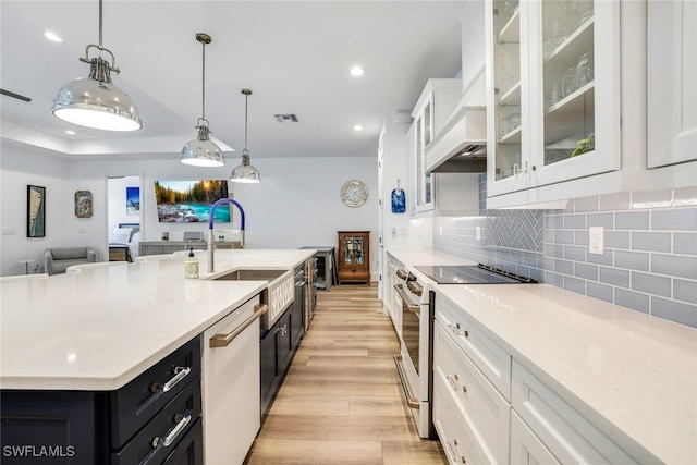 kitchen with white cabinets, appliances with stainless steel finishes, decorative light fixtures, and a kitchen island with sink