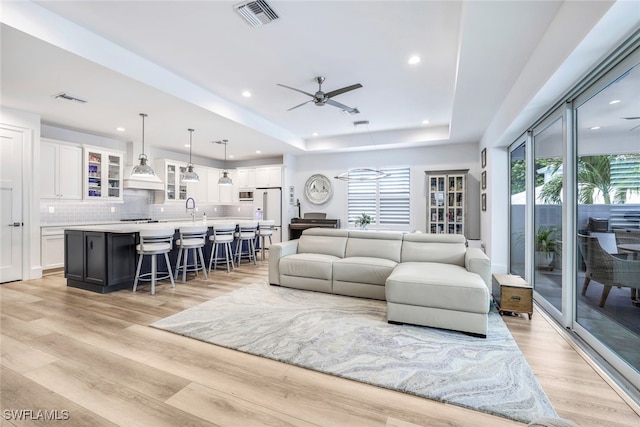 living room featuring a raised ceiling, ceiling fan, sink, and light hardwood / wood-style floors