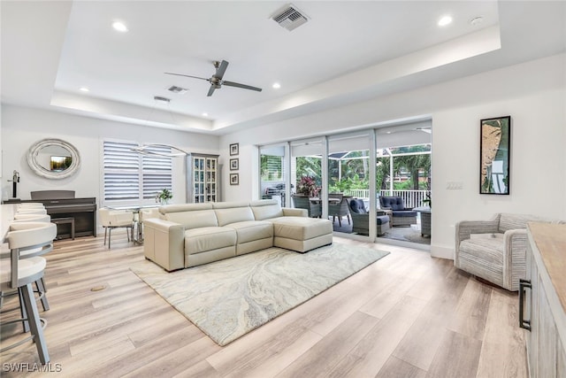 living room featuring light hardwood / wood-style floors, a raised ceiling, and ceiling fan